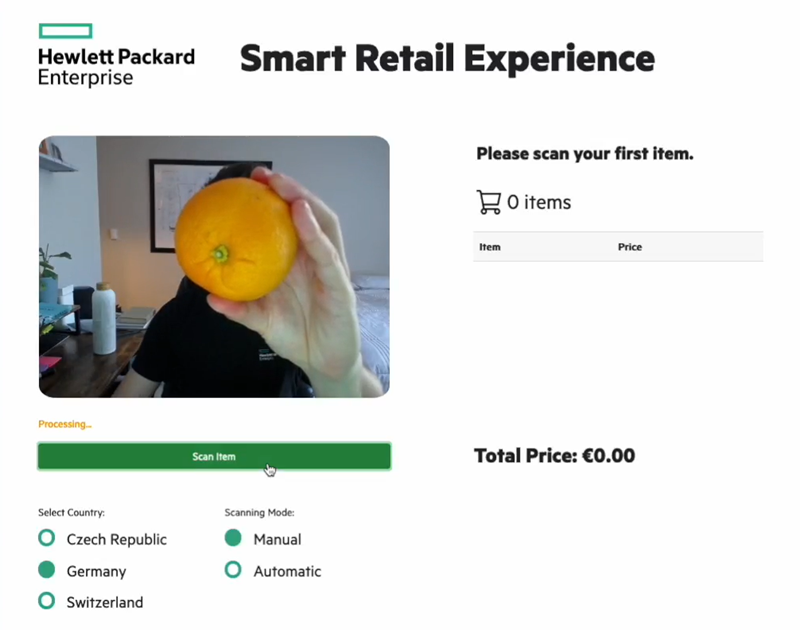 This pictures shows a human presenting an orange to a checkout webcam. 